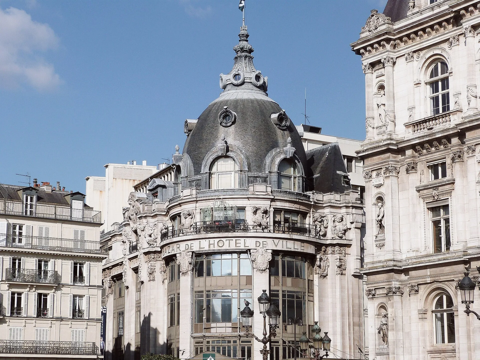 La façade du BHV, le Bazar de l'Hôtel de Ville, et sa coupole à l'angle de la rue de Rivoli à Paris, sous un ciel bleu.