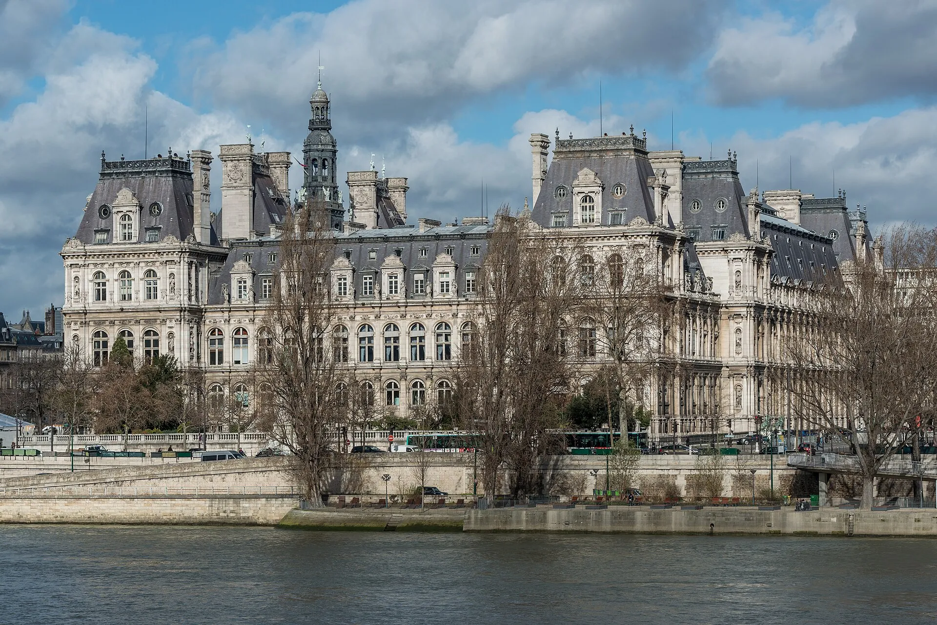 La façade de l'Hôtel de Ville de Paris vue depuis le sud, avec sa toiture d'ardoise et ses statues, sous un ciel dégagé.