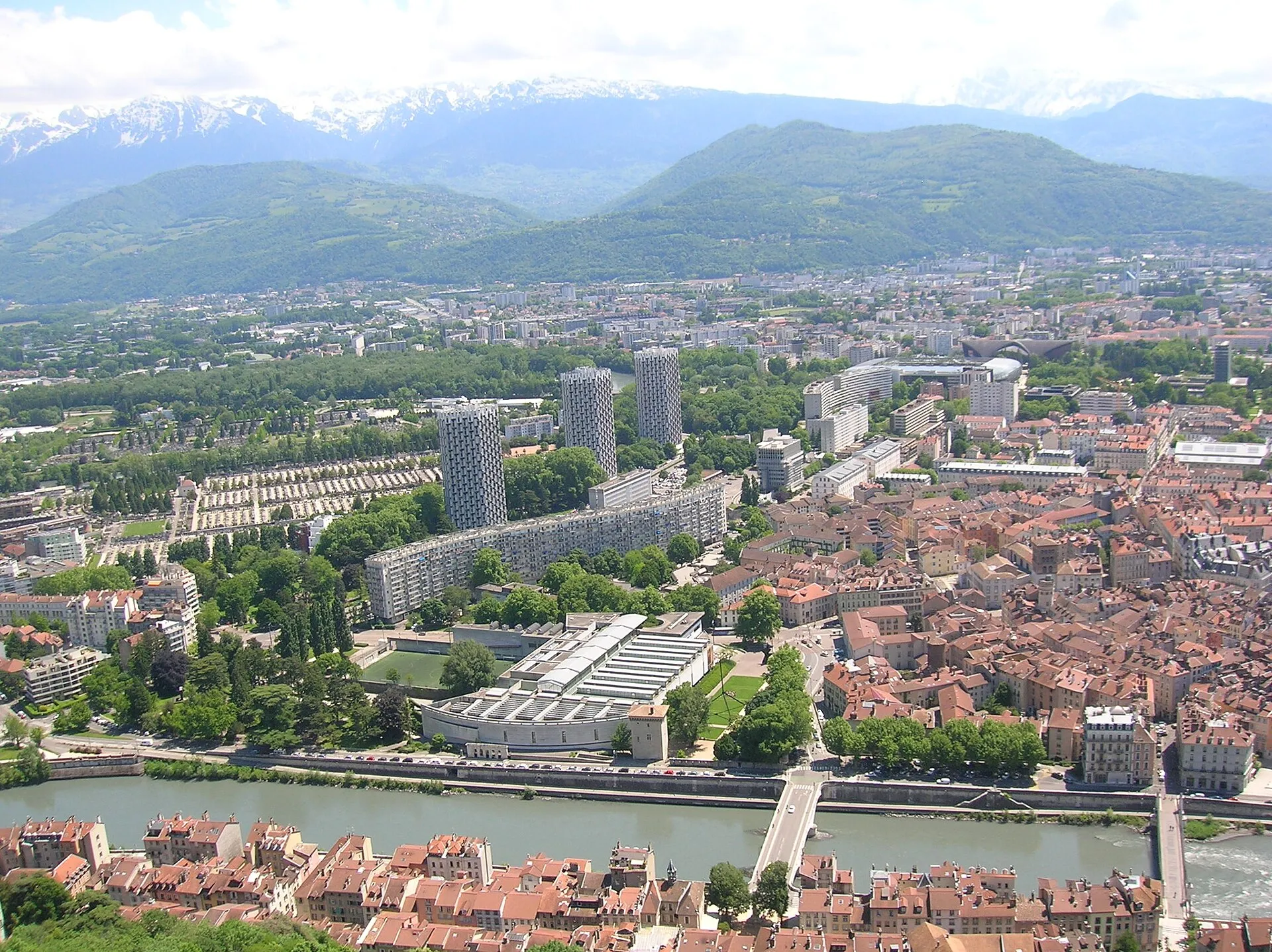 Vue de Grenoble depuis la Bastille : le quartier de l'Île Verte et ses trois tours d'habitation, l'Isère au premier plan et les montagnes en arrière-plan.
