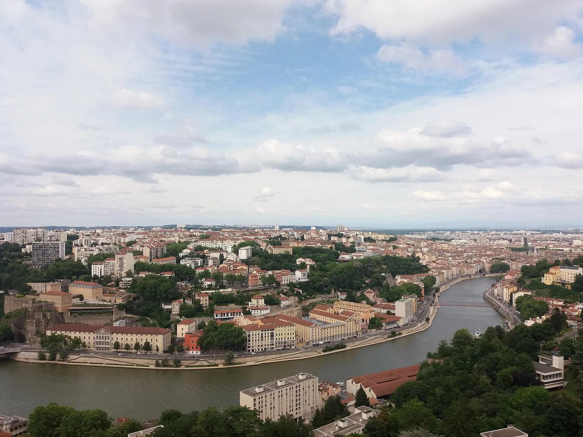 Vue en hauteur sur Lyon et la Saône, bordée d'immeubles d'habitation aux toits de tuiles, avec la ville qui s'étend jusqu'à l'horizon.
