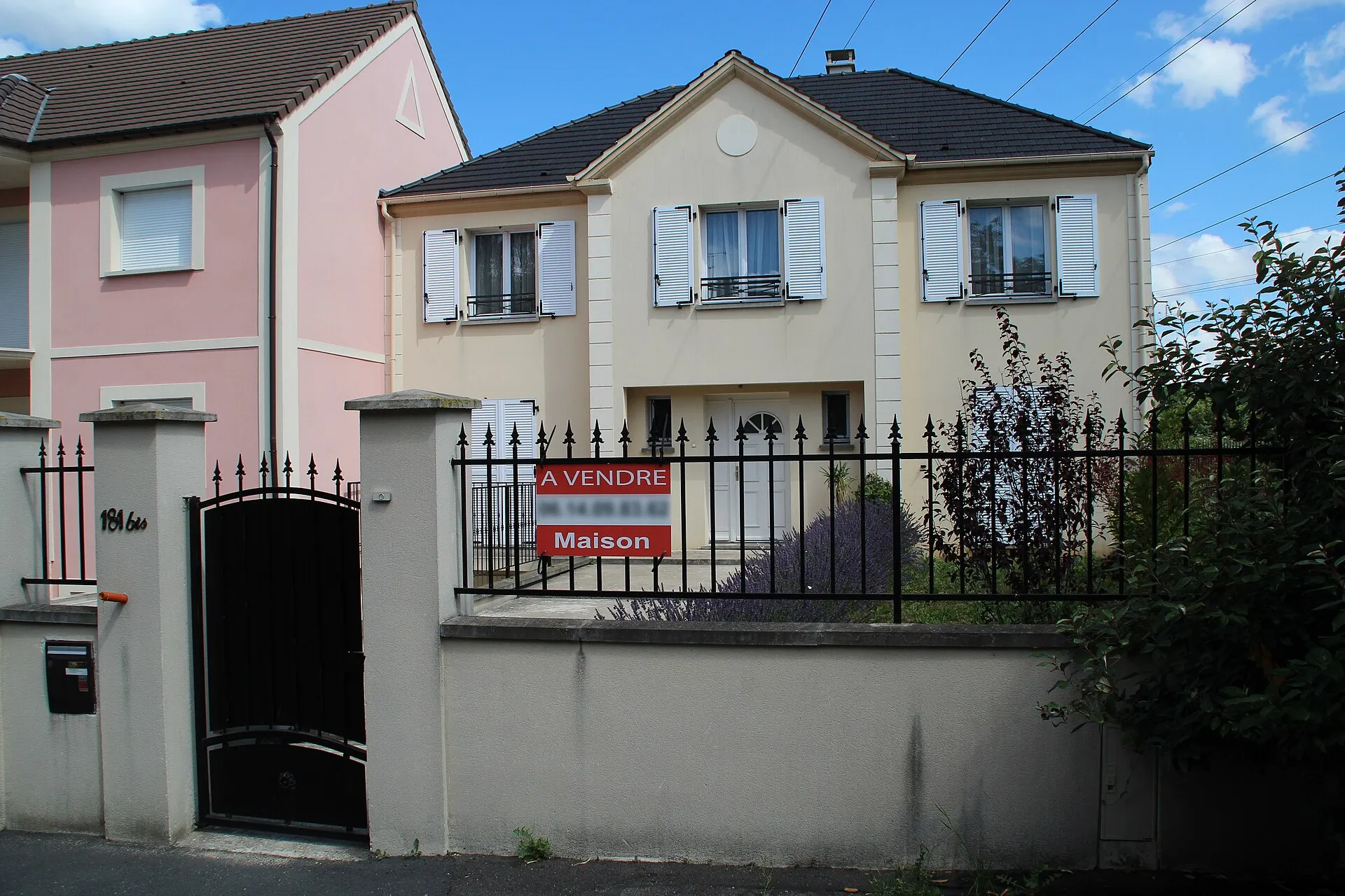 Une maison mitoyenne aux Ulis, en Essonne, avec un panneau « à vendre » d'agence immobilière accroché à la grille du jardin.