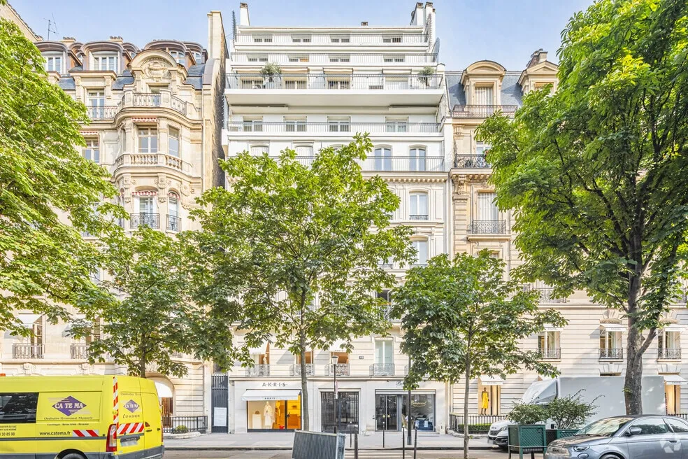 Façade haussmannienne au 49 avenue Montaigne à Paris, avec les vitrines des boutiques Akris et Bonpoint en rez-de-chaussée, derrière les arbres de l'avenue.